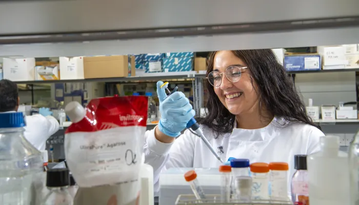 A woman with dark hair pipetting in a lab.