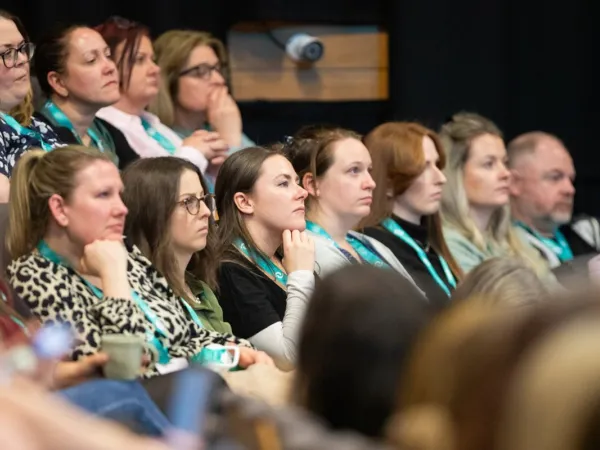  A range of people sitting in a theatre-style seating arrangement, intently listening to an out-of-shot speaker.