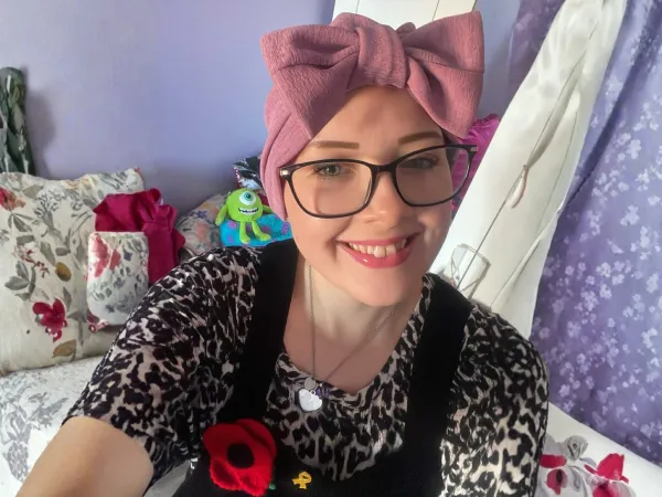 A young woman is taking a selfie, she is smiling and wearing a headband with a large pink bow.