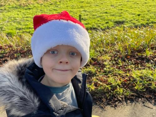 A young boy, Wilf, walking outdoors with a red and white Christmas hat on
