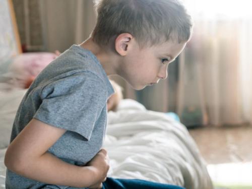 A young boy sitting on his bed and holding his stomach in pain