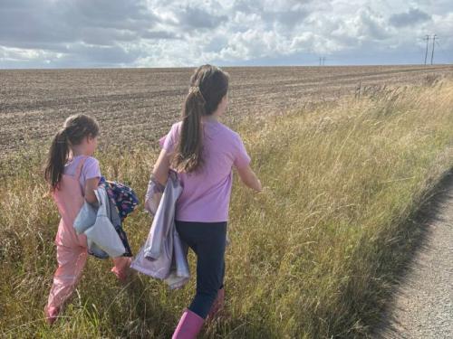 2 young girls dressed in pink, walking through a field on a cloudy day