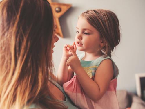 A woman holding her daughter up close to her face. Mum and daughter are both smiling.