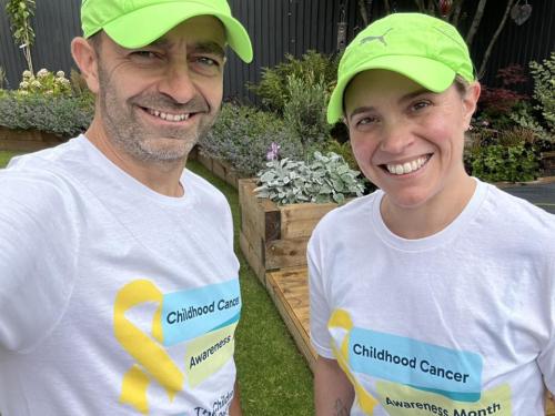 A man and woman wearing white t-shirts with the CCLG and Childhood Cancer Awareness logos, smiling at the camera