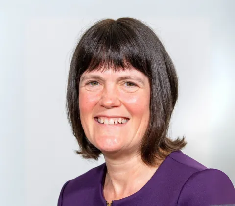 A headshot of a woman with shoulder-length brown hair, smiling and wearing a purple shirt.