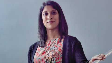 Shaarna smiling at the camera with mid-length dark brown hair and wearing a colourful patterned blouse.