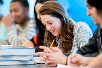 Smiling young people sitting at a table with books and pencils.