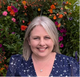 A headshot of a woman with shoulder length blonde hair, smiling, wearing a blue shirt.