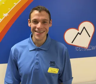 A man in a blue NHS Scotland uniform smiling at the camera.