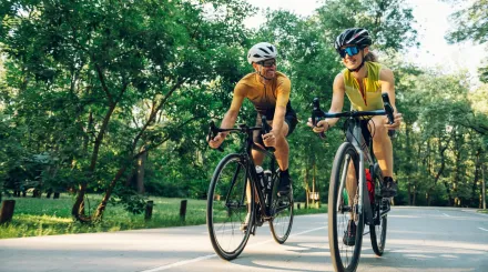 Two cyclists, a man and a woman, dressed in yellow cycling gear, cycling along a road and smiling
