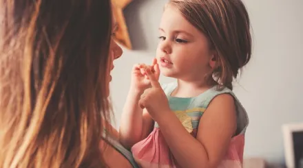 A woman holding her daughter up close to her face. Mum and daughter are both smiling.