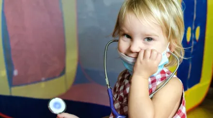 A young girl playing with a stethescope and smiling at the camera
