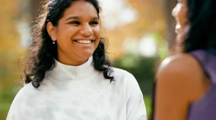 Indian girl with white blouse and shoulder length black hair smiling and talking to another Indian girl 