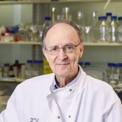 Mel in his lab. He is wearing a white lab coat and glasses, and is smiling at the camera.