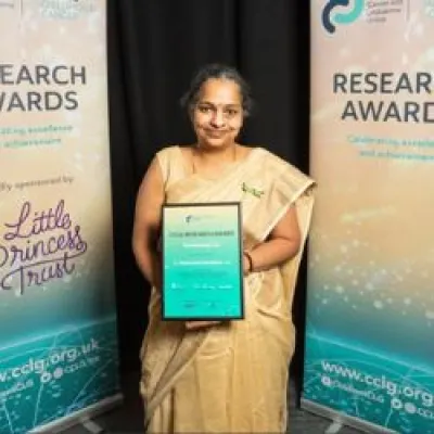 Madhumita holding a certificate whilst smiling at the camera and wearing a gold saree.