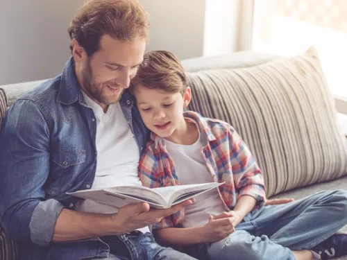 A man and boy seated on a sofa reading a book together