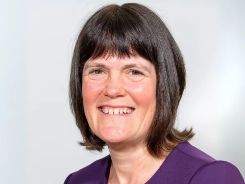 A headshot of a woman with shoulder-length brown hair, smiling and wearing a purple shirt.