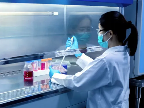 A female researcher pipetting liquids in a research laboratory, whilst wearing a lab coat and gloves.