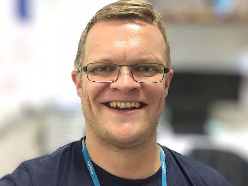 Robin smiling at the camera, wearing a navy t-shirt and glasses.