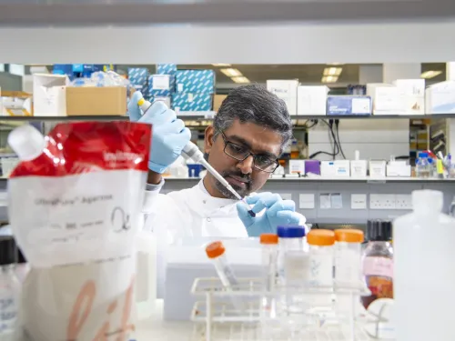 A male researcher pipetting in the lab, surrounded by boxes of research materials.