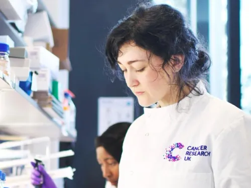 Jess working in the lab, wearing a lab coat and purple gloves.