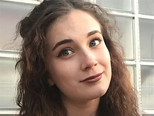 Lauren smiling at the camera. She has dark, curly hair and is wearing a black tank top.