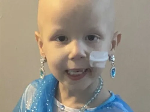 A young girl with a nasogastric tube is smiling at the camera while wearing a blue princess costume.