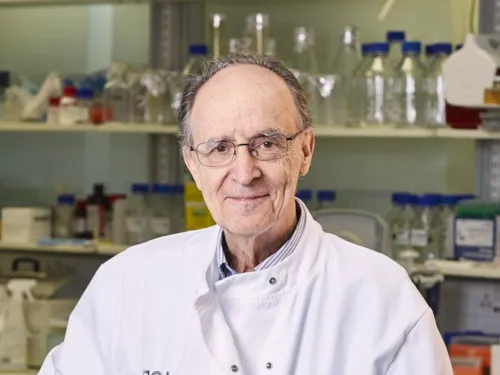 Mel in his lab. He is wearing a white lab coat and glasses, and is smiling at the camera.