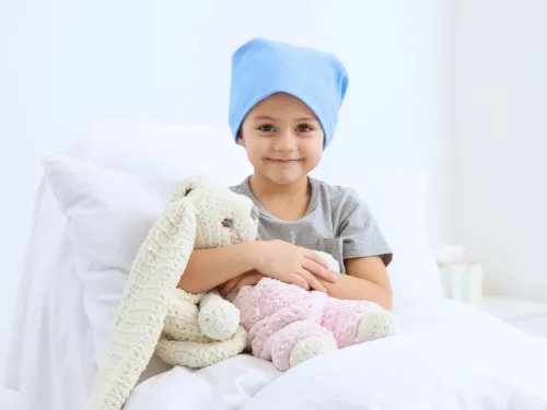 A girl in a hospital bed wearing a blue hat and cuddling a knitted white rabbit toy.