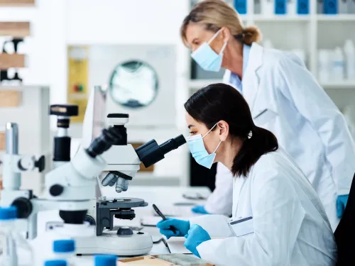 Two female researchers in lab coats using microscopes.