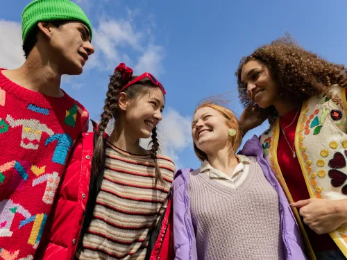 Four teenagers in bright clothes standing in front of a blue sky.