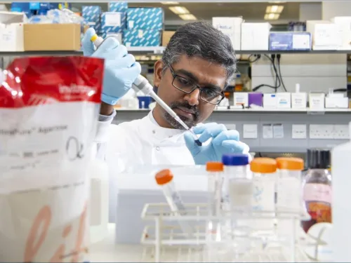 Anand pipetting in the lab, surrounded by boxes and test tubes.