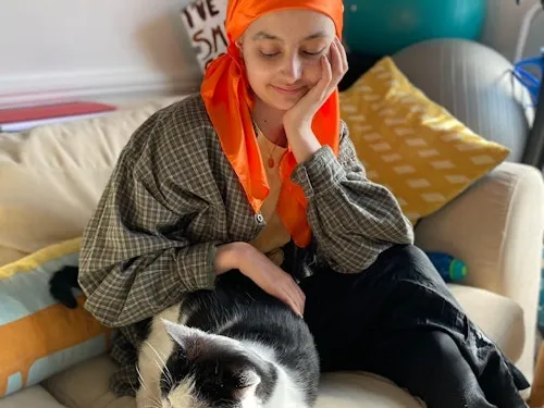 Ruby Fuller wearing an orange head scarf and stroking a black and white cat.