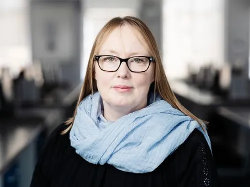 Suzanne, smiling at the camera with dark blonde hair. She is wearing a black top and light blue scarf.