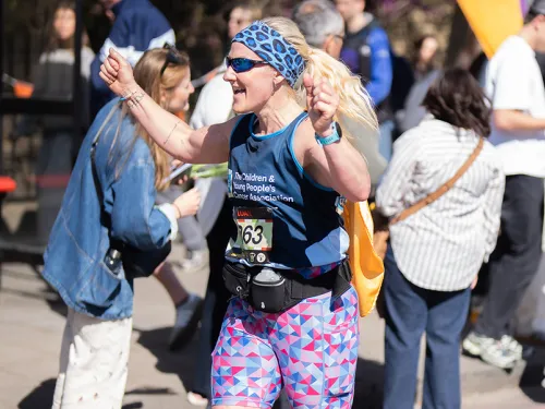 A woman running a marathon, smiling and holding her fists in the air as she runs past other people