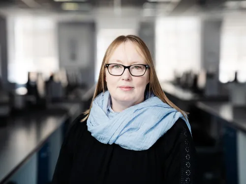 Suzanne smiling at the camera with straight blonde hair, wearing a blue scarf and black top.