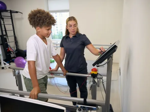 A child in hospital with a physiotherapist, walking on a treadmill.
