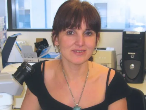Majlinda Lako, sat in her office and wearing a black blouse and blue necklace, with her dark hair in a ponytail.