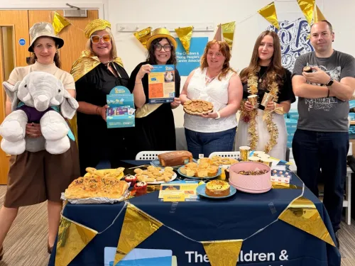 A group of CCLG staff, 5 women and one man, standing behind a table cover in cakes and smiling