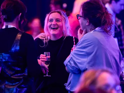 Three women laughing in a dark room with one woman holding a glass of wine