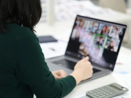woman with black hair wearing green jumper sitting at desk in an online meeting 